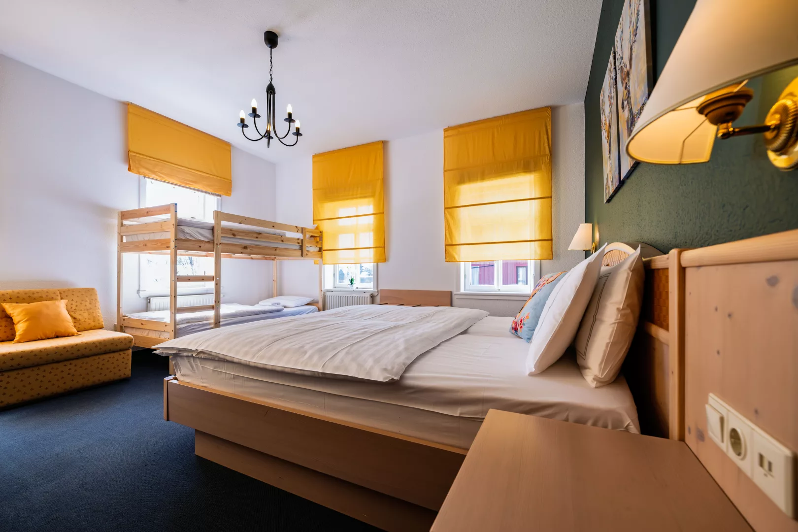 Viebettzimmer des Hotels Landidyll mit Doppelbett, Etagenbett aus Holz und einem Schlafsofa, Nachttischen und grüner Wand mit Bildern