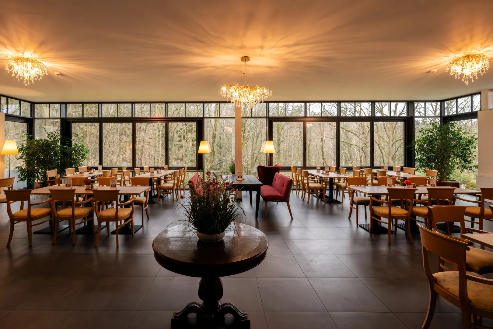 Wintergarten im Parkhotel Hohnstein mit großer Fensterfront mit Blick in den Wald, vielen Tischen und Stühlen und Dekoration