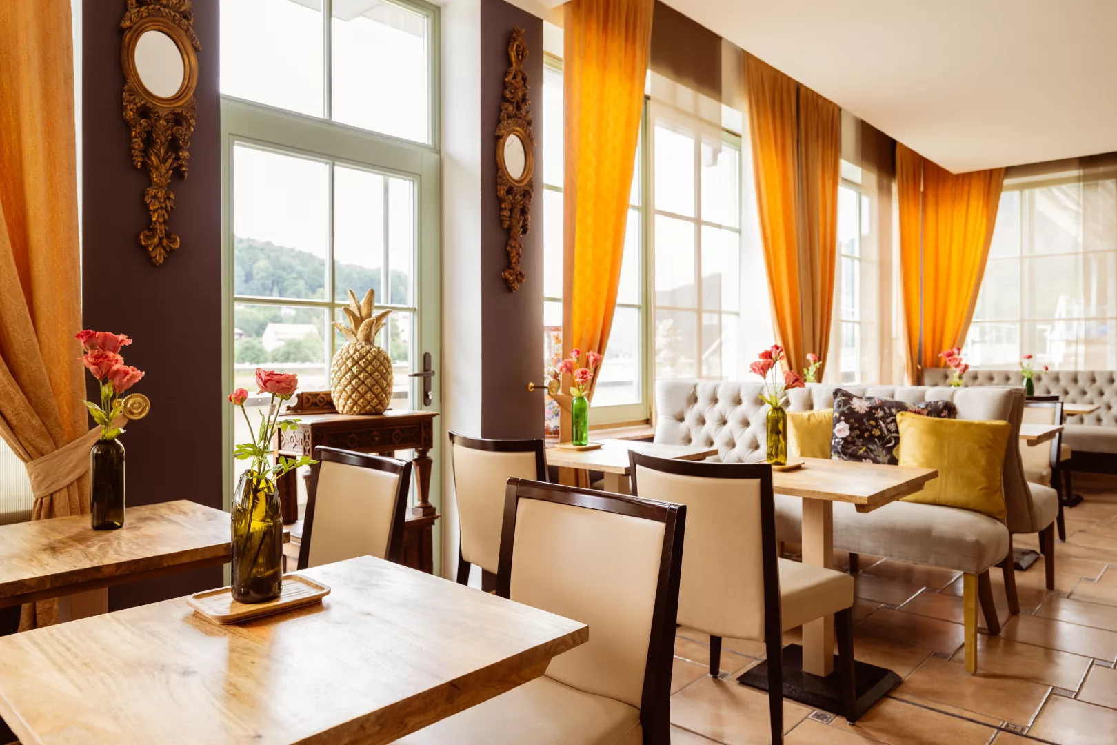 Restaurant im Hotel Zeitgeist mit modernen Bänken und Stühlen, Tischen und frischen Blumen, Dekoration und hellen Vorhängen vor einer lila Wand
