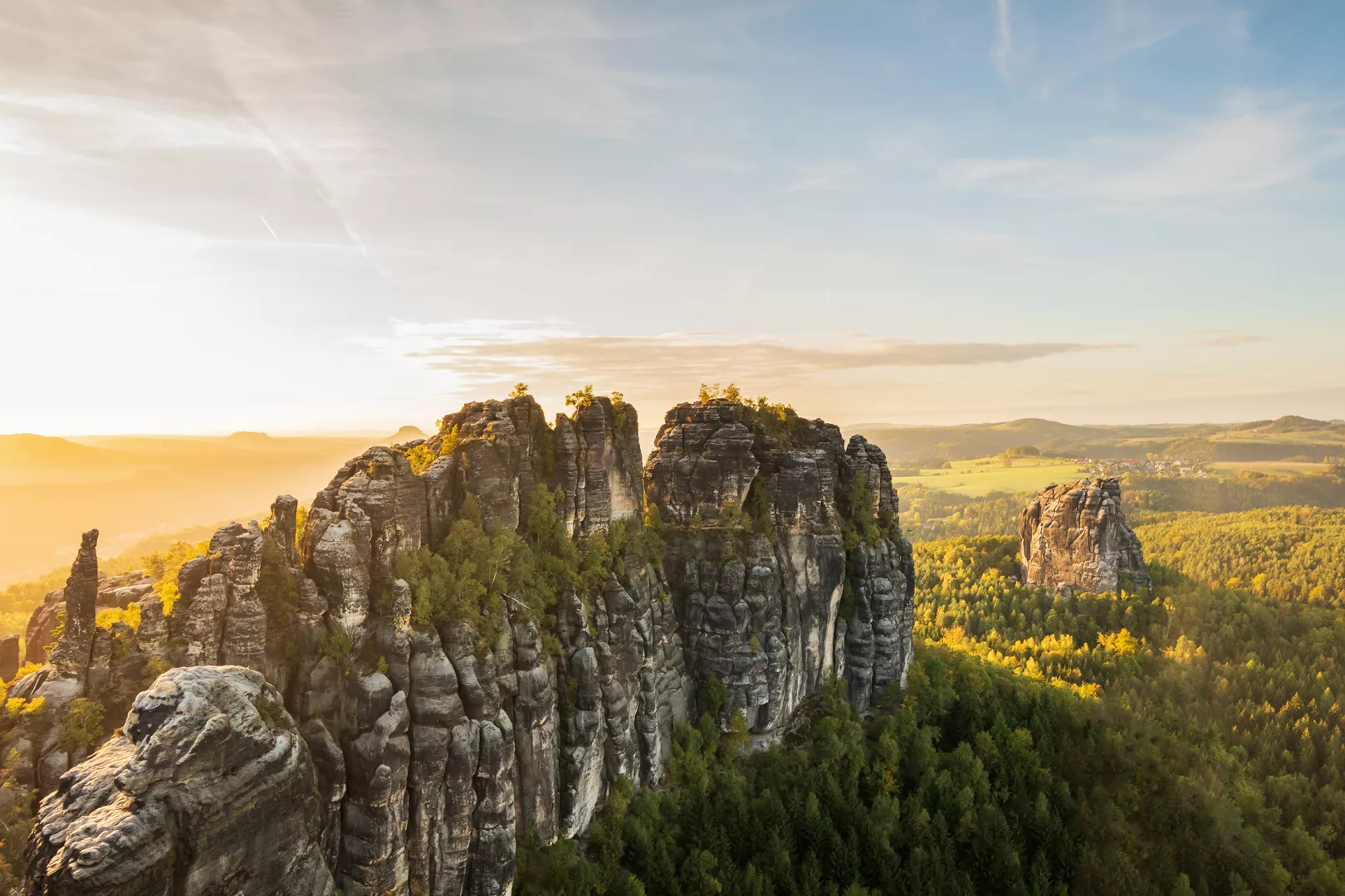 Blick auf die Schrammsteine in der Sächsichen Schweiz bei Sonnenuntergang im Sommer, mit grünen Feldern im Hintergrund