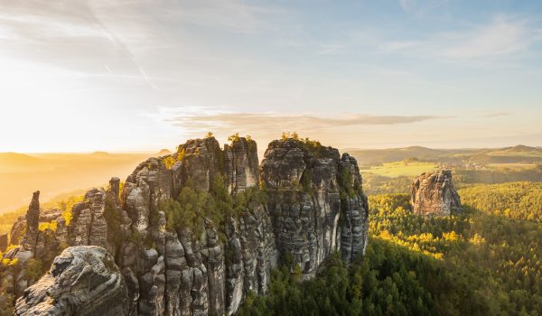 Blick auf die Schrammsteine in der Sächsichen Schweiz bei Sonnenuntergang im Sommer, mit grünen Feldern im Hintergrund